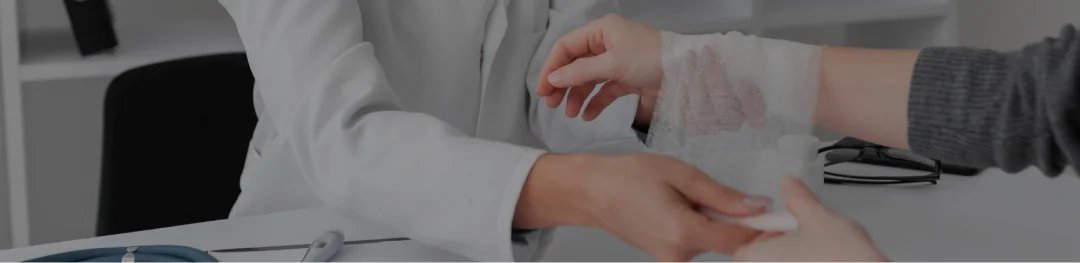  A person carefully applies bandages to another person's injured hand, demonstrating care and attention to first aid.